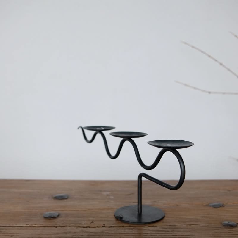 Black metal Three-Candle Holder with wavy design on wooden surface.